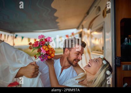 close up of a young beardy man carrying  his bride inside of the camper, smiling, laughing, just married Stock Photo