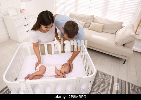 Happy couple near crib with their cute baby at home Stock Photo