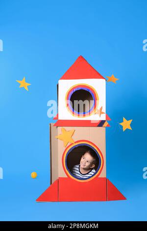 Cute little boy playing with cardboard rocket on light blue background Stock Photo