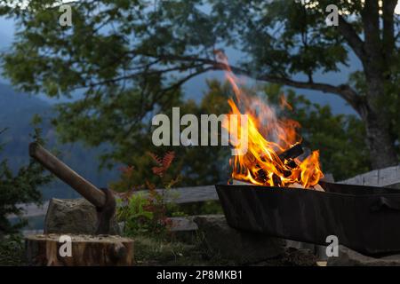 Metal brazier with burning firewood on backyard in mountains Stock Photo