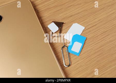 SIM cards, mobile phone and ejector tool on wooden table, flat lay Stock Photo