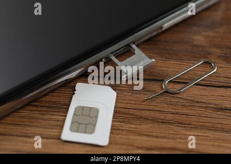 SIM card, mobile phone and ejector tool on wooden table, closeup Stock Photo