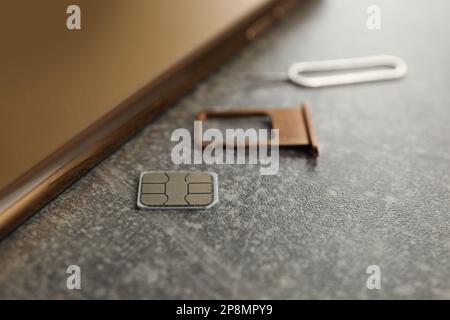 SIM card, mobile phone, tray and ejector tool on grey table, closeup Stock Photo