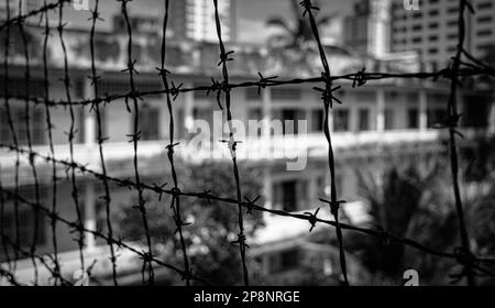 Looking through barbed wire at the notorious Tuol Sleng S-21 torture and genocide prison museum in Phnom Penh, Cambodia. More than 18,000 people died Stock Photo
