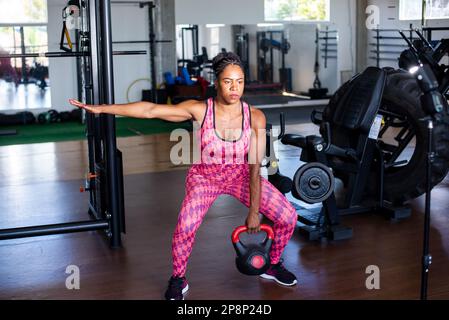 Determined Woman Doing Squat Exercises With Kettlebell. Spine strengthening. Stock Photo