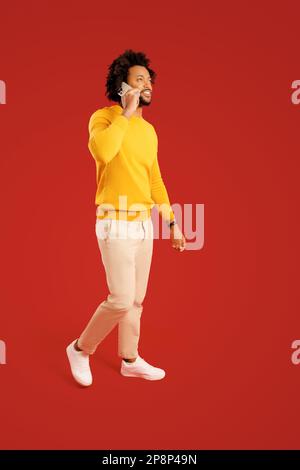 Handsome young 30s man talking phone, calling to discuss plans, looking away with dreamy facial expression. Indoor studio shot isolated on red background Stock Photo