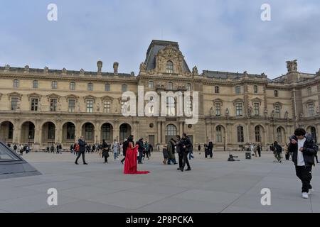 Couple in red getting photographed outside the Louvre museum with tourists around Stock Photo