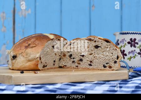 Giant hot cross bun on a chopping board. Traditional spiced, sticky glazed fruit buns with pastry crosses. Served as a classic Easter treat. Stock Photo