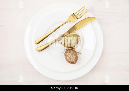 Easter table setting, Golden Easter eggs decoration, napkin and gold cutlery on plates, white wooden table, Stock Photo