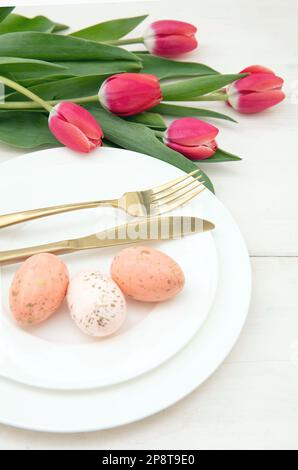 Easter table setting, Spring flowers and eggs decoration, golden cutlery on plates, white background Stock Photo