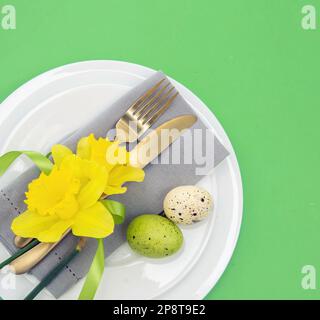 Easter table setting, Spring flowers and eggs decoration, napkin and golden cutlery on white plates, pastel green background Stock Photo