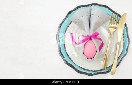 Easter table setting and decoration, Easter egg in a gray napkin, golden cutlery on plates set, white background Stock Photo