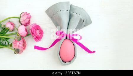 Easter table setting, Pink Easter egg in a gray napkin, rabbit ears shape on white wooden background, top view Stock Photo
