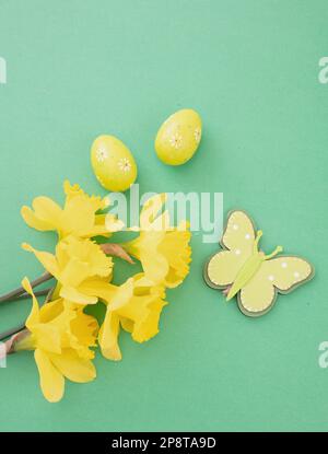 Easter eggs, yellow daffodils flowers bunch, Spring season decoration on green background, top view Stock Photo