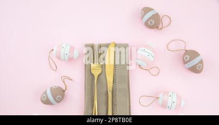 Easter table setting, Easter eggs decoration, napkin and golden cutlery on pastel pink background, top view Stock Photo
