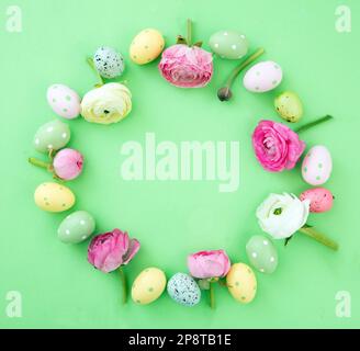Easter egg and Spring flowers decoration wreath on green pastel background, top view, copy space. Happy Easter card template. Stock Photo