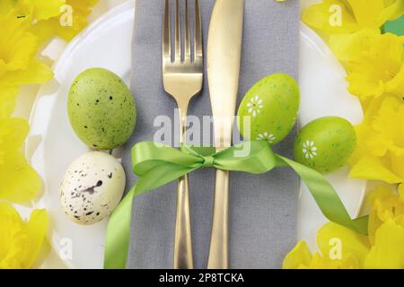 Easter table setting, Yellow Spring flowers and eggs decoration, napkin and golden cutlery on white plates, close up top view Stock Photo