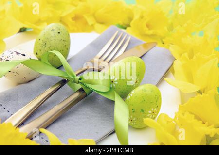Easter table setting, Yellow Spring flowers and eggs decoration, napkin and golden cutlery on white plates, close up view Stock Photo