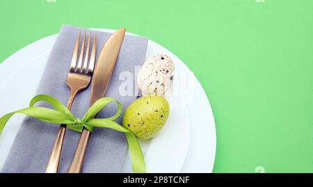 Easter table setting, Easter eggs decoration, napkin and golden cutlery on white plates, pastel green background Stock Photo