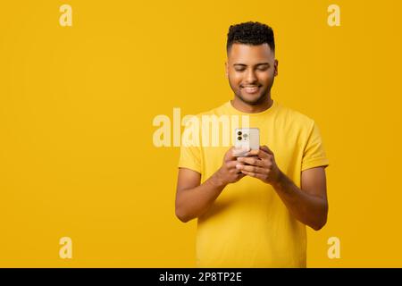 Young Indian 20s man is using his smartphone, sending text messages or browsing the web, enjoying his time using various mobile applications to chat with friends and stay connected online, isolated Stock Photo
