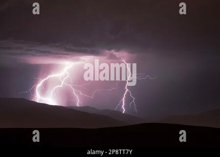 A dramatic image of a stormy sky above a mountain range, illuminated by a brilliant lightning bolt Stock Photo