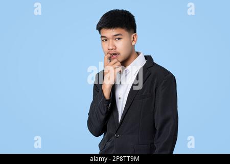 Young handsome asian businessman in panic, worry and scared face isolated on blue light background Stock Photo
