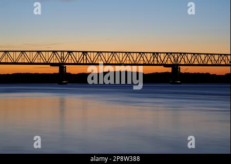 An aerial view of a bridge illuminated by a stunning sunset over a large blue body of water Stock Photo