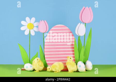 Felt spring flowers and wooden Easter egg with chicks in front of blue background Stock Photo