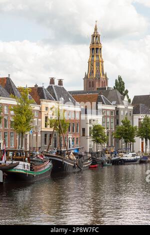 Historic ships, canal houses and warehouses on the old harbor at the Hoge der A with the tower of the historic Der Aa church in Groningen. Stock Photo