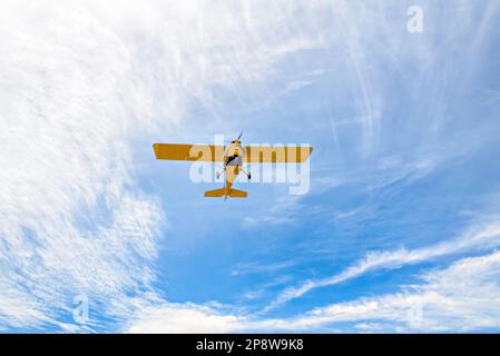 Yellow single-engine ultralight airplane flying in the blue sky with white clouds Stock Photo