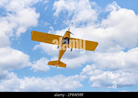 Yellow single-engine ultralight airplane flying in the blue sky with white clouds Stock Photo