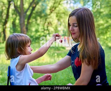 A cute child treats his beloved mother with a sweet cherry berry in nature Stock Photo