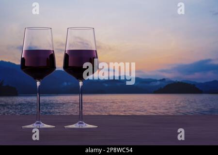 Two glasses of red wine with view of sunset over lake and mountains. Stock Photo