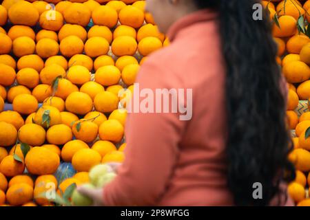 oranges kinnu citrus fruit piled up at a roadside stall showing how farmers traditionally sell this local fruit with out of focus woman buying it Stock Photo