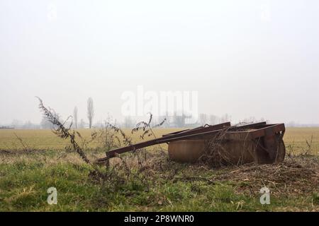 Rusty  steamroller lying next to a cultivated field on a misty day in winter Stock Photo