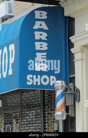 New York, NY - June 13, 2021: Local barber shop store front with pole in New York City community. Vertical orientation. Stock Photo