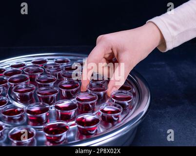 Closeup of young woman taking communion the wine symbol of Jesus Christ blood in small cups on black background. Easter Passover and Lord Supper conce Stock Photo