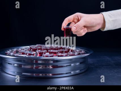 Closeup of young woman taking communion the wine symbol of Jesus Christ blood in small cups on black background. Easter Passover and Lord Supper conce Stock Photo