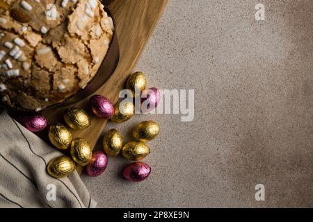 Easter cake or bread kulich with almond and sugar with chocolate Easter eggs on wooden cutting board, striped napkin . Happy Easter holiday concept, r Stock Photo