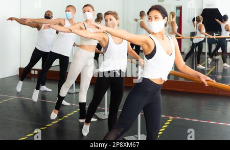 Group of men and women in protective masks practicing at ballet barre Stock Photo