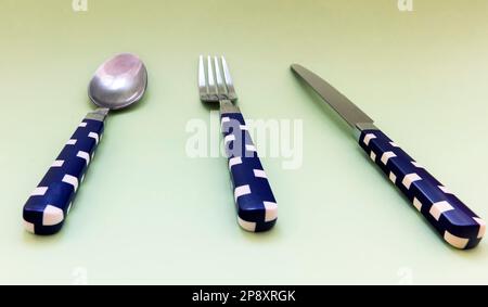 Blue and white check pattern spoon, fork, knife on green background Stock Photo