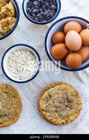 Chocolate chip cookies laid out with enamel bowls filled with the recipe ingredients. Eggs, flour, sugar, chocolate. Stock Photo