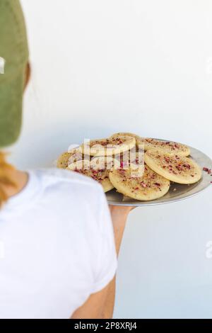 A baker holds a tray of cookies seen over her shoulder on a simple white background. Stock Photo