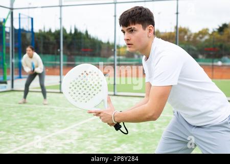Guy hitting two handed backhand during paddle tennis match Stock Photo