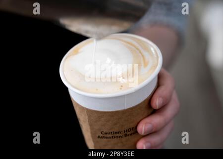 Espresso in a white paper cup with steamed milk being poured on top Stock Photo