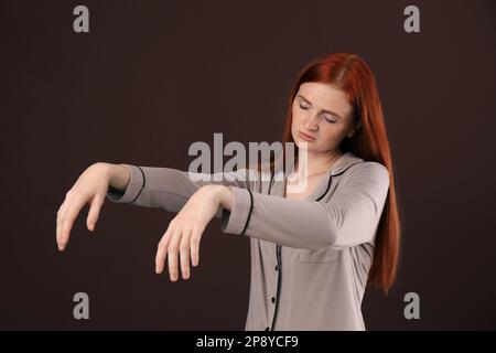 Young woman wearing pajamas in sleepwalking state on brown background Stock Photo