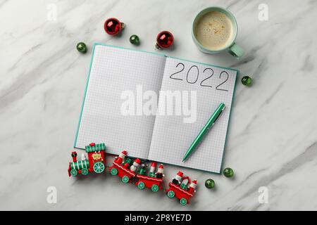 Open planner, cup of coffee and Christmas decor on white marble background, flat lay. 2022 New Year aims Stock Photo
