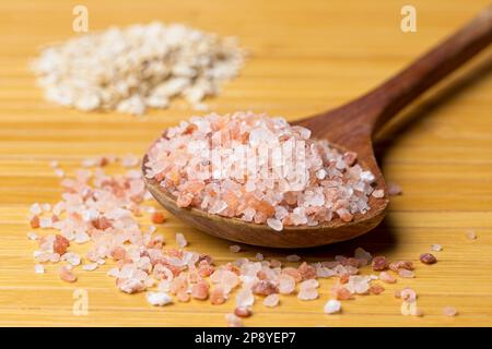 A close up studio photo of coarse pink himalayan se salt on a wooden spoon and a pile of dried oats in the background. Stock Photo
