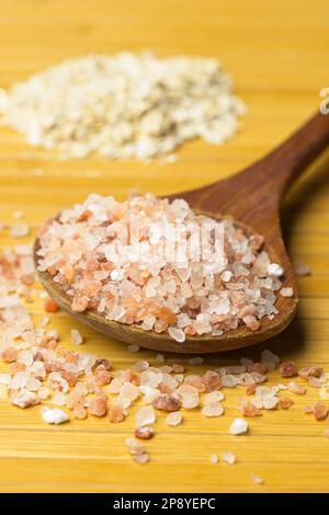 A close up studio photo of coarse pink himalayan se salt on a wooden spoon and a pile of dried oats in the background. Stock Photo