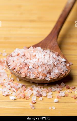 A close up  photo of pink Himalayan sea salt on a wooden spoon and on a table. Stock Photo